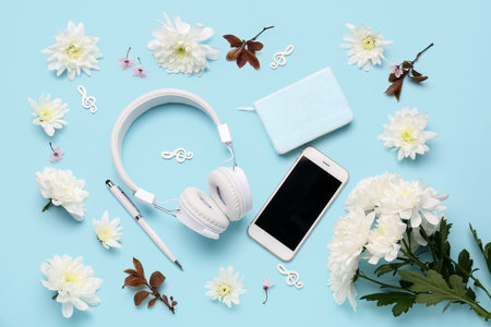 Composition with modern headphones, mobile phone, notebook and beautiful flowers on color background