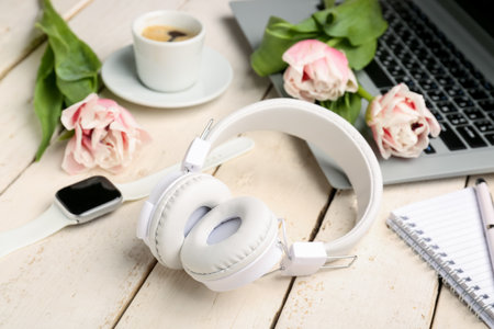 Modern headphones, wristwatch, laptop, cup of coffee and tulip flowers on light wooden backgroundの写真素材
