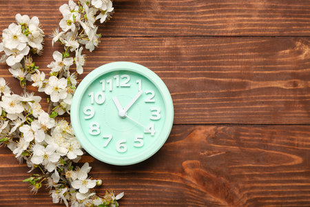 Blooming spring branches and clock on wooden background