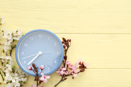 Blooming spring branches and blue clock on yellow wooden backgroundの写真素材