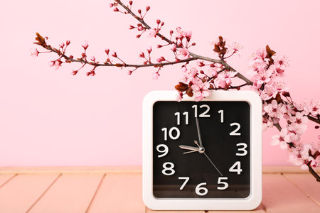 Blooming spring branches and clock on pink wooden tableの写真素材