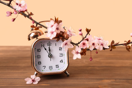 Blooming spring branches and golden alarm clock on wooden table