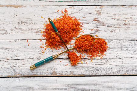 Spoons with pile of saffron on white wooden background