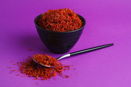 Bowl and spoon with pile of saffron on purple backgroundの写真素材