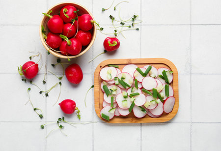 Board and bowl with fresh slices of radish on light tile backgroundの写真素材