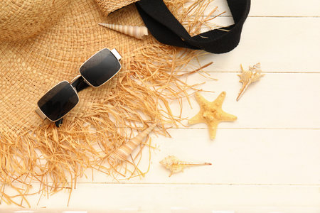 Composition with sunglasses, straw hat, starfish and seashells on white wooden background