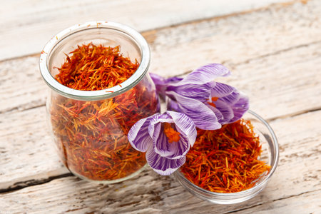 Jar and bowl of dried saffron threads with crocus flowers on white wooden tableの写真素材
