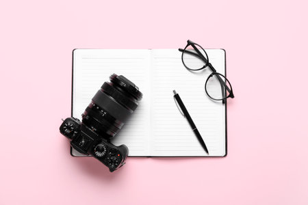 Notebook with pen, eyeglasses and photo camera on pink background