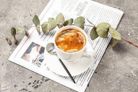 Cup of coffee with spoon, eucalyptus branch and newspaper on grunge backgroundの写真素材