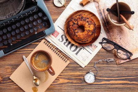 Cup of coffee with notebook, typewriter, newspaper, bun and map on wooden backgroundの写真素材