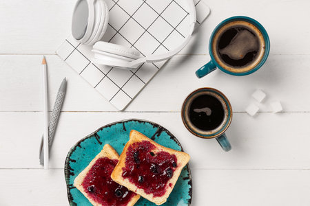 Cups of coffee with toasts, headphones and stationery on white wooden backgroundの写真素材