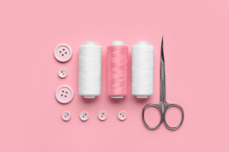Composition with thread spools, buttons and scissors on pink backgroundの写真素材