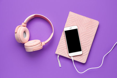 Headphones with mobile phone and notebook on purple backgroundの写真素材