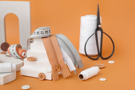 Podiums with tailor's supplies on orange background, closeup