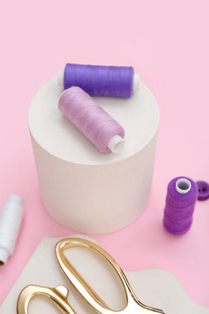 Podium with thread spools on pink background, closeup