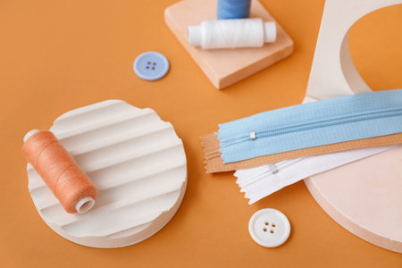 Podiums with thread spools, buttons and zips on orange background, closeup