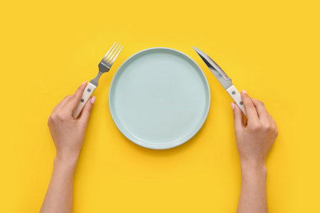 Woman with cutlery and empty plate on yellow backgroundの写真素材