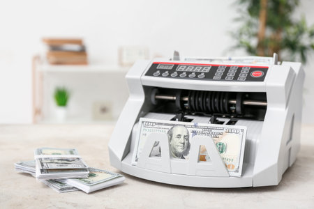 Modern cash counting machine with dollar banknotes on table in room