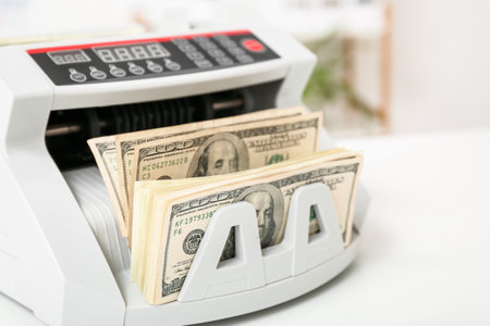Modern cash counting machine with dollar banknotes on table in office, closeupの写真素材