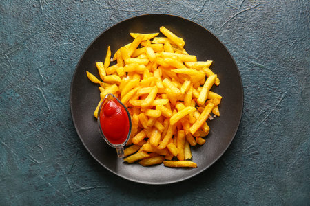 Plate with tasty french fries and ketchup on dark color background