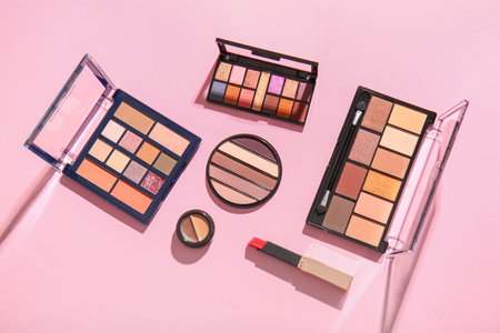 Different palettes of eye shadows and lipstick on pink background