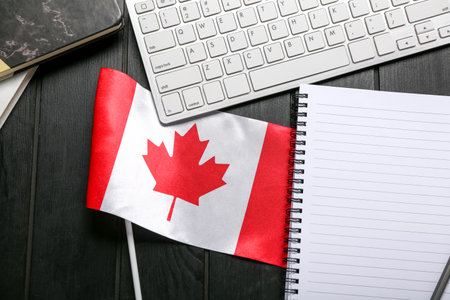 Canadian flag with notebook and computer keyboard on dark wooden background, closeupの写真素材