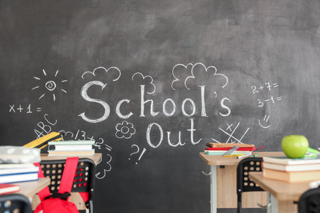 Text SCHOOL'S OUT with drawings on blackboard in classroomの写真素材