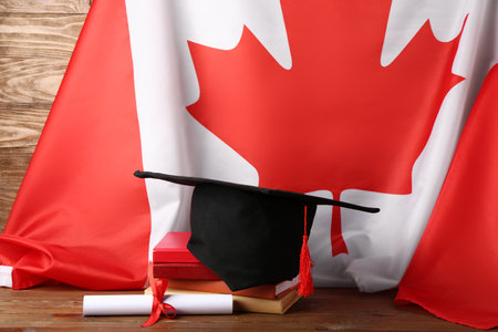 Graduation hat with diploma, books and flag of Canada on wooden tableの写真素材