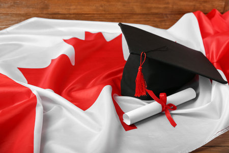 Graduation hat with diploma and flag of Canada on wooden background, closeupの写真素材