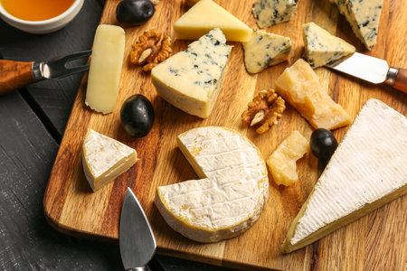 Wooden board with different types of tasty cheese on table, closeup