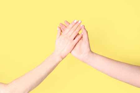 Women holding hands together on yellow background. friendship conceptの写真素材