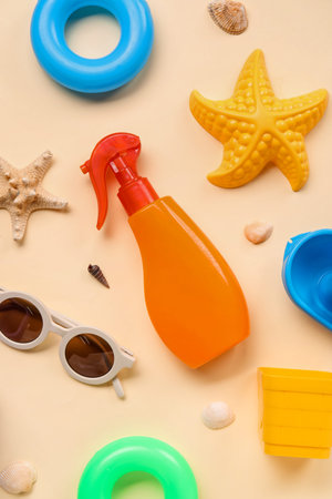 Sunscreen cream for baby with beach accessories and seashells on beige background