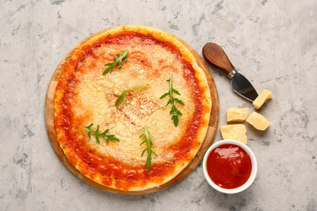 Wooden board of tasty pizza with parmesan cheese and tomato sauce on gray grunge backgroundの写真素材