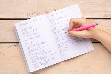 Woman writing maths formulas in copybook with pen on beige wooden backgroundの写真素材