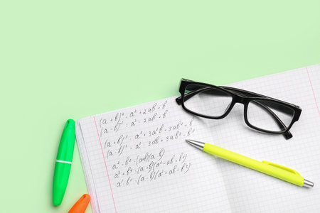 Copybook with maths formulas, glasses and stationery on green backgroundの写真素材