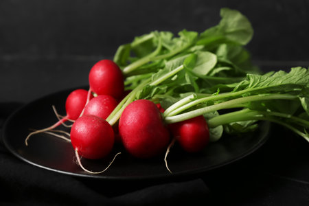 Plate of ripe radish with green leaves on dark background, closeupの写真素材