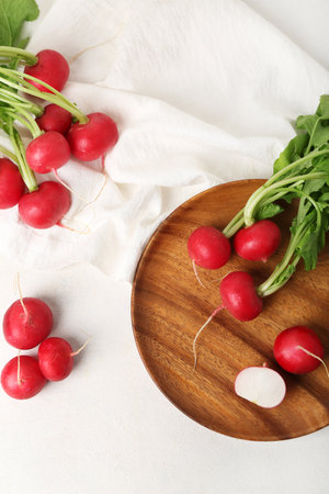Plate of ripe radish with green leaves on light backgroundの写真素材