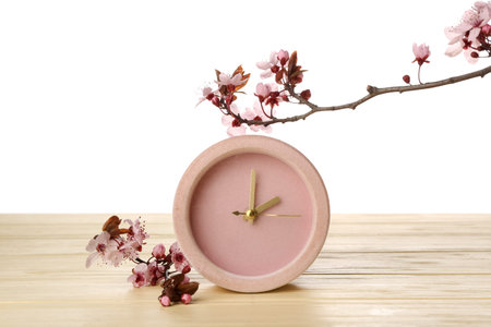 Blooming spring branches and clock on table against white background