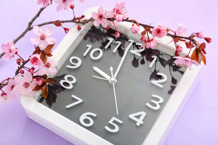 Blooming spring branches and clock on lilac background