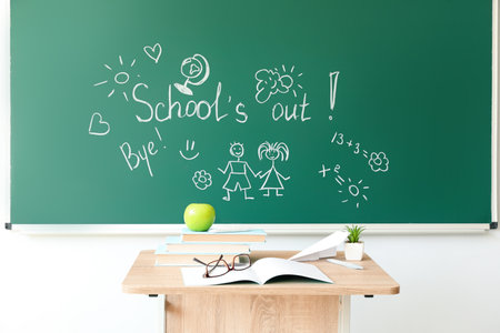 Text SCHOOL'S OUT with drawings on blackboard in classroomの写真素材