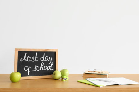 Chalkboard with text LAST DAY OF SCHOOL, apples and notebooks on table near light wallの写真素材