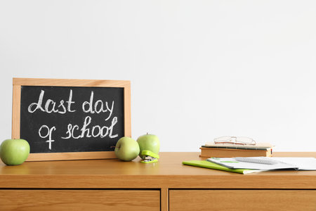 Chalkboard with text LAST DAY OF SCHOOL, apples and notebooks on table near light wallの写真素材