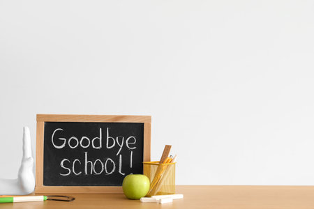 Chalkboard with text GOODBYE SCHOOL, apple and stationery on table near light wallの写真素材