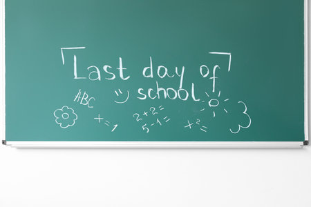 Blackboard with text LAST DAY OF SCHOOL and drawings on white wallの写真素材