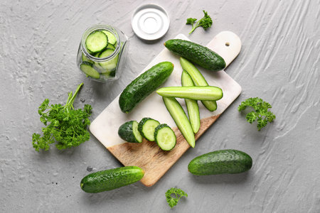 Board and jar with fresh cucumbers on gray backgroundの写真素材