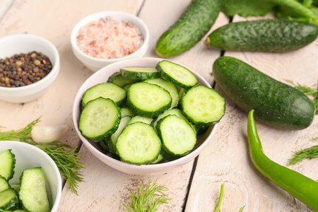 Bowl with pieces of fresh cucumber on light wooden backgroundの写真素材