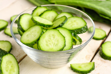 Bowl with pieces of fresh cucumber on light wooden backgroundの写真素材