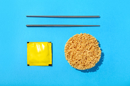 Raw instant noodles with metal chopsticks and seasoning on blue backgroundの写真素材