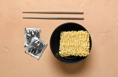Raw instant noodles in bowl with chopsticks and seasoning on beige backgroundの写真素材