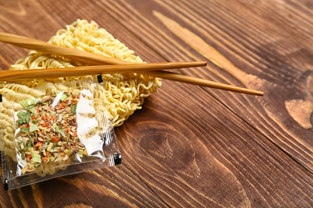 Raw instant noodles with seasoning and chopsticks on wooden background, closeupの写真素材